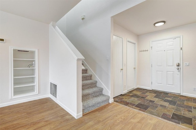 entrance foyer featuring dark wood-style flooring, visible vents, stairway, and baseboards