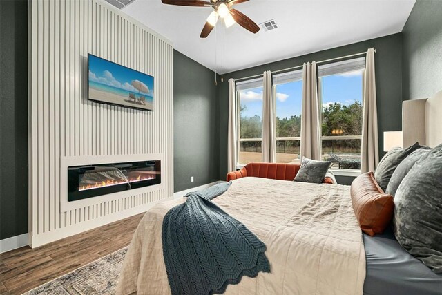 bedroom with a glass covered fireplace, visible vents, baseboards, and wood finished floors