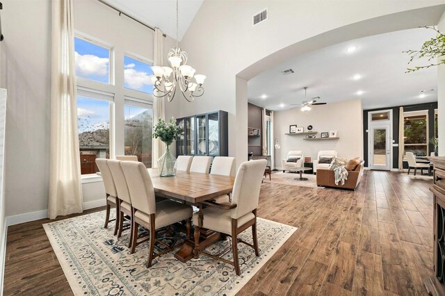 dining space with arched walkways, high vaulted ceiling, wood finished floors, and visible vents