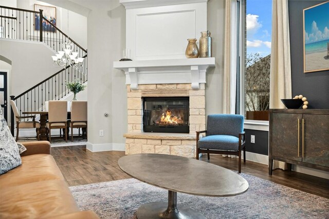 living area with a stone fireplace, dark wood-type flooring, stairway, and baseboards