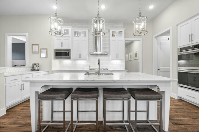 kitchen featuring white cabinetry, a center island with sink, glass insert cabinets, and stainless steel appliances