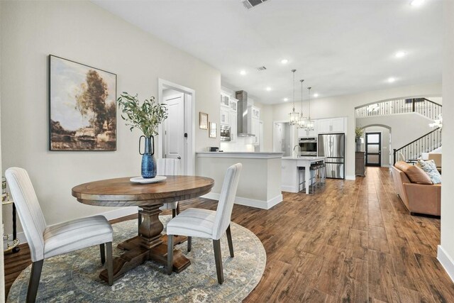 dining area featuring arched walkways, stairway, wood finished floors, an inviting chandelier, and recessed lighting