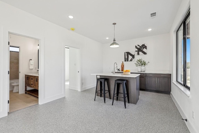 kitchen with light countertops, hanging light fixtures, visible vents, a sink, and an island with sink