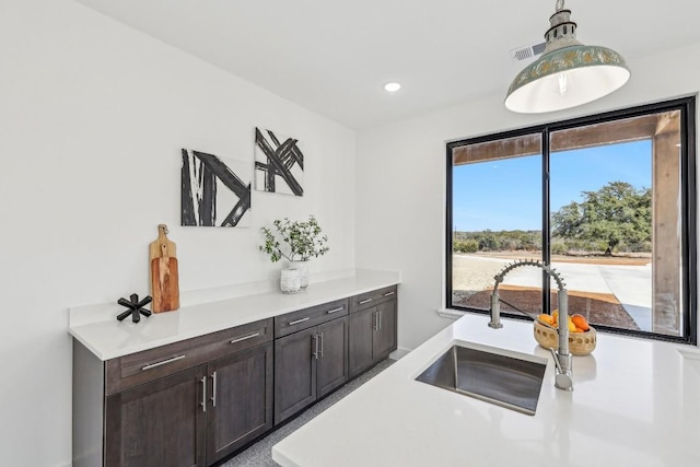 kitchen with visible vents, hanging light fixtures, light countertops, dark brown cabinets, and a sink