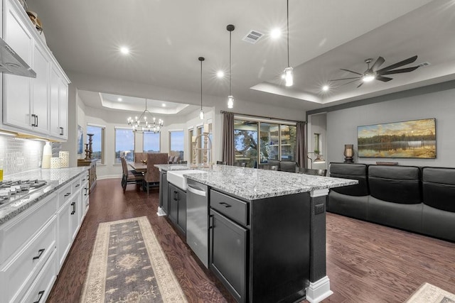 kitchen featuring a tray ceiling, a center island with sink, stainless steel appliances, open floor plan, and white cabinets