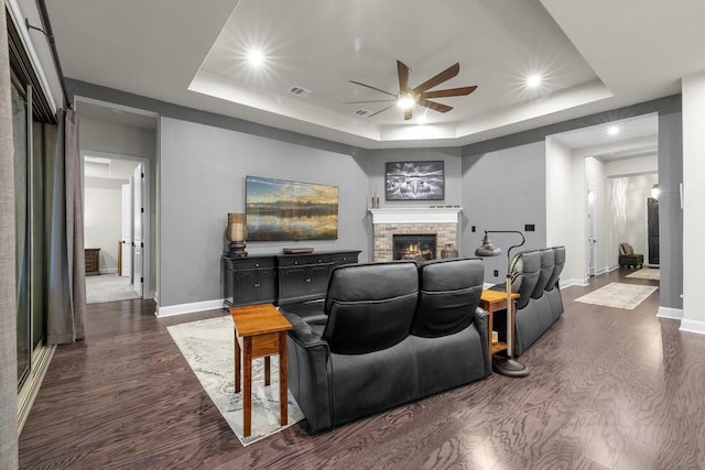 living room featuring dark wood-style floors, visible vents, a fireplace, and a tray ceiling