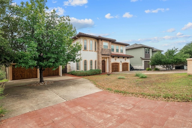 mediterranean / spanish house featuring stucco siding, stone siding, driveway, a tiled roof, and a front lawn