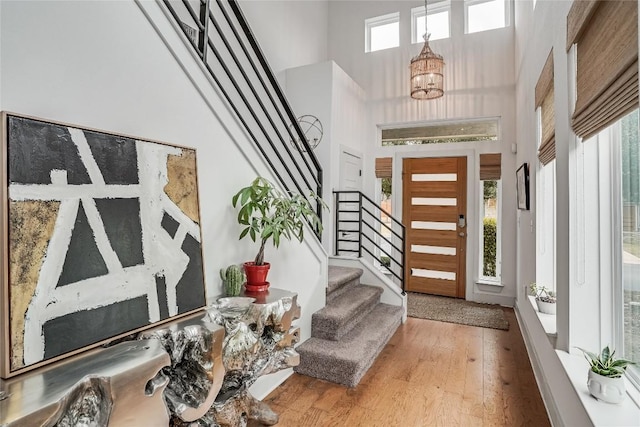 foyer featuring stairs, wood finished floors, a towering ceiling, and a chandelier