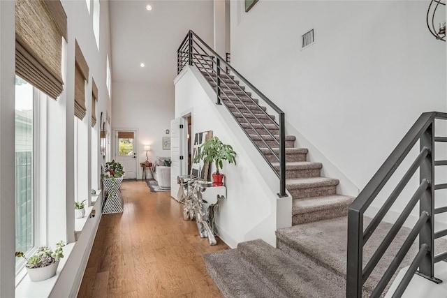 foyer entrance featuring a towering ceiling, stairs, visible vents, and wood finished floors