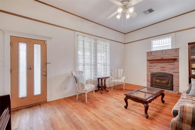 living room with a fireplace, visible vents, baseboards, ornamental molding, and light wood finished floors