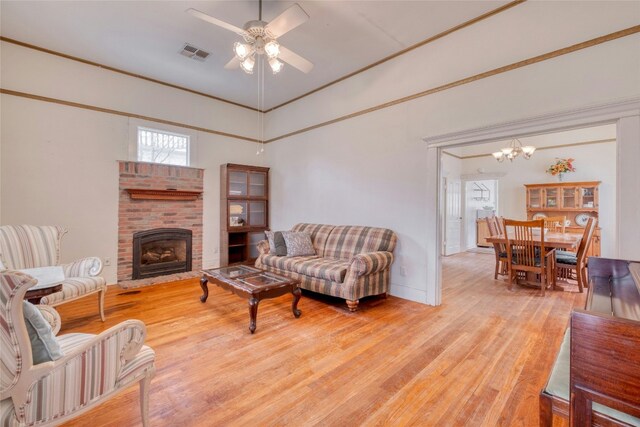 living room with ceiling fan with notable chandelier, light wood finished floors, a brick fireplace, and visible vents