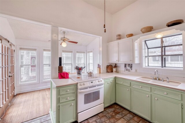 kitchen with green cabinetry, a peninsula, light countertops, white electric range, and a sink