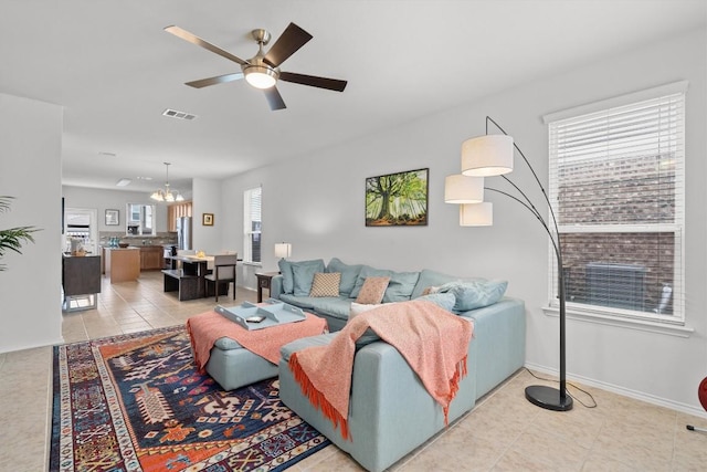 living room with ceiling fan with notable chandelier, light tile patterned floors, visible vents, and baseboards