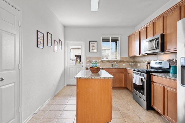 kitchen with appliances with stainless steel finishes, a center island, light tile patterned floors, and light stone countertops