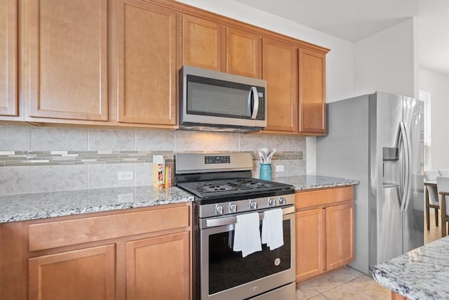 kitchen with stainless steel appliances, decorative backsplash, light stone counters, and light tile patterned floors