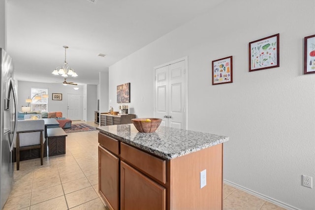 kitchen with a center island, decorative light fixtures, open floor plan, light stone countertops, and stainless steel fridge