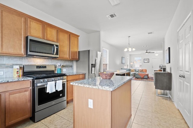 kitchen with light tile patterned floors, stainless steel appliances, a kitchen island, open floor plan, and light stone countertops