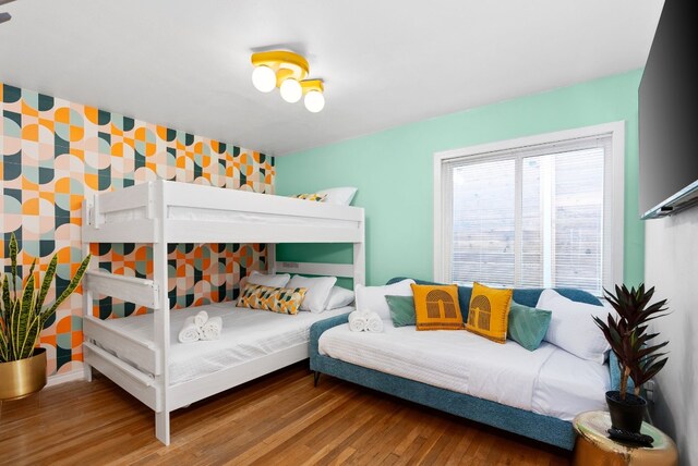 bedroom featuring an accent wall, wallpapered walls, and wood finished floors