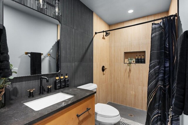 bathroom with toilet, tiled shower, vanity, and decorative backsplash