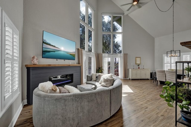 living area with a glass covered fireplace, wood finished floors, french doors, high vaulted ceiling, and ceiling fan with notable chandelier