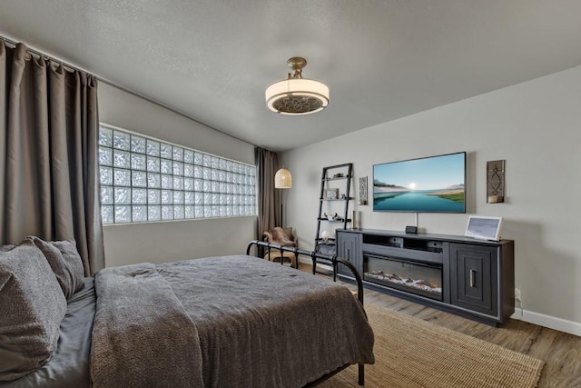 bedroom with a glass covered fireplace, light wood-style flooring, and baseboards