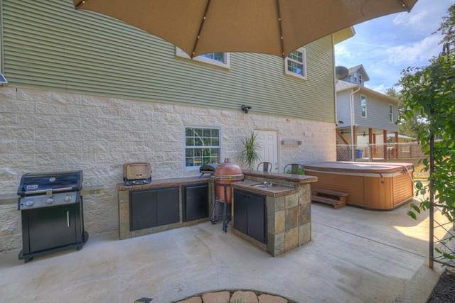 view of patio with a hot tub, fence, exterior kitchen, and area for grilling