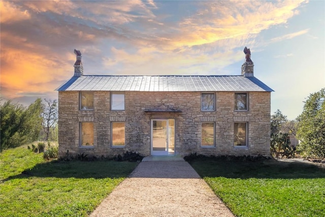 view of front of property featuring a chimney, metal roof, and a front yard