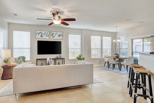 living room with ceiling fan with notable chandelier, light tile patterned flooring, visible vents, and baseboards