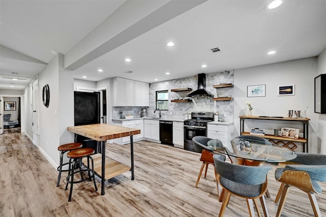 3010 Burleson Rd Unit A, Austin, TX 78741 - kitchen with black appliances, wall chimney range hood, decorative backsplash, light wood-style flooring, and white cabinetry