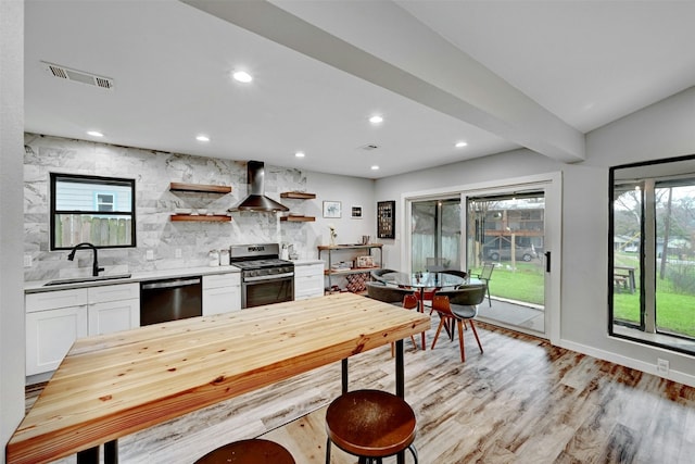 3010 Burleson Rd Unit A, Austin, TX 78741 - kitchen with stainless steel appliances, wall chimney exhaust hood, white cabinetry, light wood-style floors, and backsplash