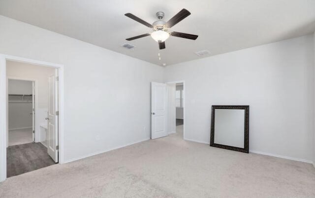 unfurnished bedroom featuring visible vents, light colored carpet, ceiling fan, a walk in closet, and a closet