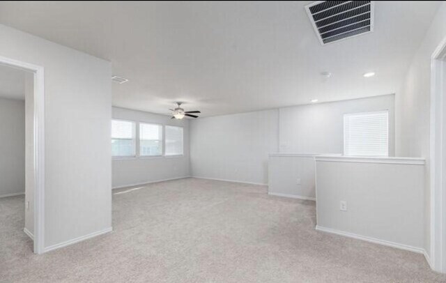 spare room with light carpet, baseboards, visible vents, and a ceiling fan