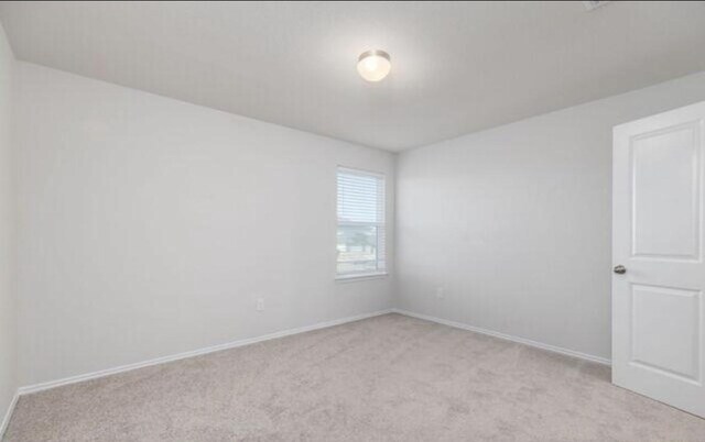 empty room featuring light carpet and baseboards