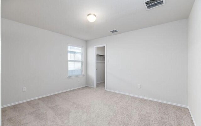 unfurnished bedroom featuring light carpet, a walk in closet, visible vents, and baseboards