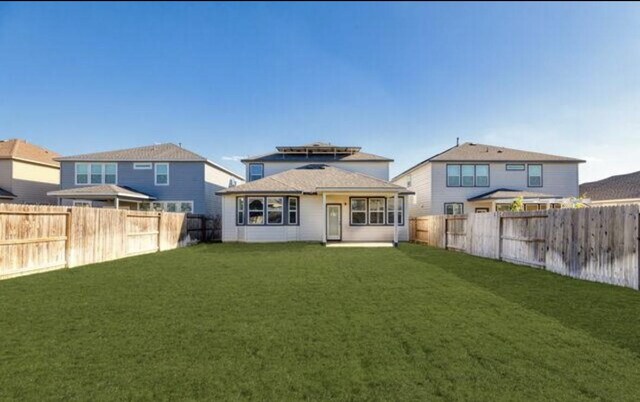 back of property with a fenced backyard and a lawn