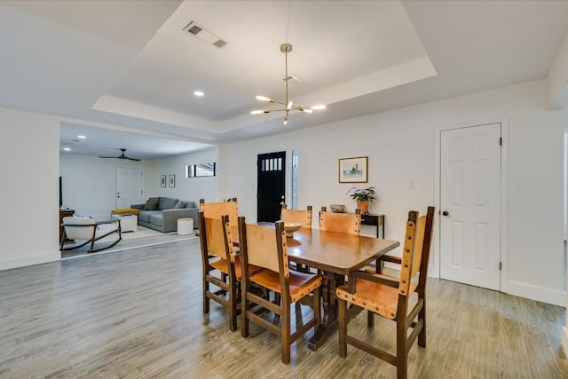 dining room with light wood-style flooring, visible vents, a raised ceiling, and baseboards