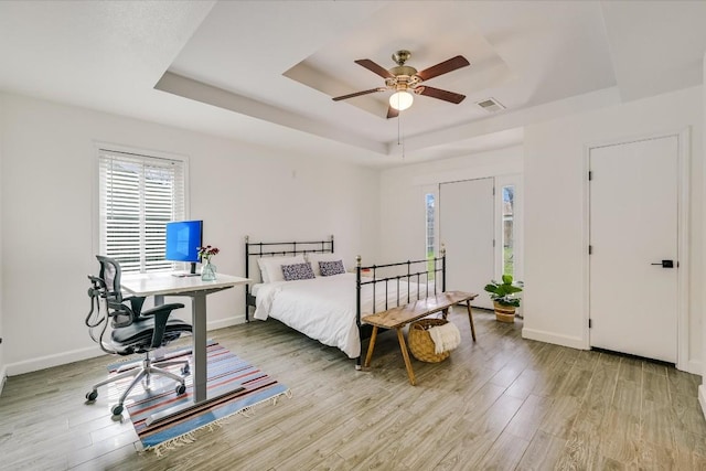 bedroom with a tray ceiling, baseboards, visible vents, and light wood finished floors