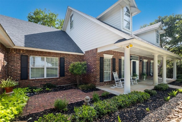 rear view of property featuring covered porch, a shingled roof, and brick siding