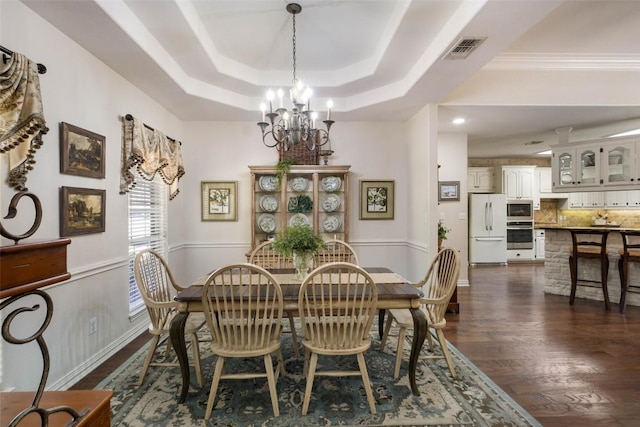 dining area featuring a tray ceiling, crown molding, dark wood finished floors, visible vents, and an inviting chandelier