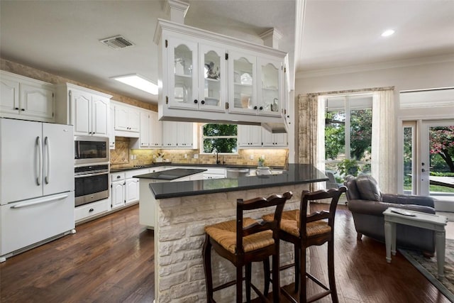 kitchen with a breakfast bar area, stainless steel appliances, visible vents, white cabinets, and glass insert cabinets