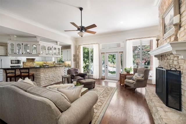 living area featuring ceiling fan, a stone fireplace, dark wood-style flooring, and crown molding