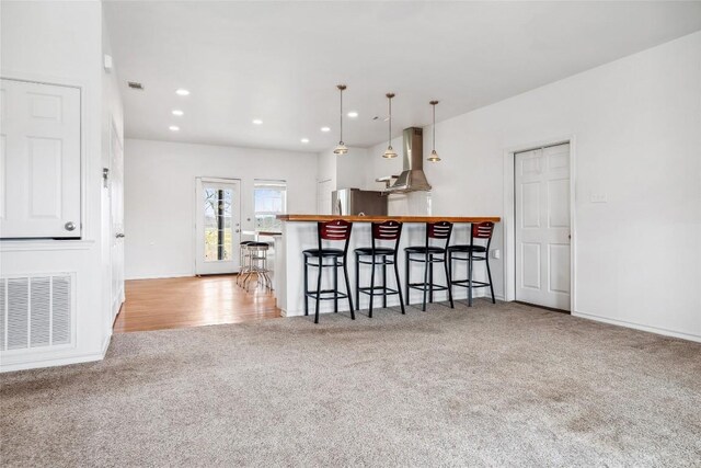 826 Savannah Cv, Elgin, TX 78621 - kitchen featuring carpet floors, freestanding refrigerator, a kitchen breakfast bar, wall chimney range hood, and decorative light fixtures