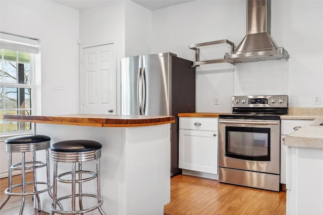 826 Savannah Cv, Elgin, TX 78621 - kitchen featuring appliances with stainless steel finishes, wall chimney exhaust hood, white cabinets, light wood-style flooring, and a kitchen breakfast bar