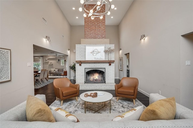 living room featuring a towering ceiling, a fireplace, a notable chandelier, and wood finished floors