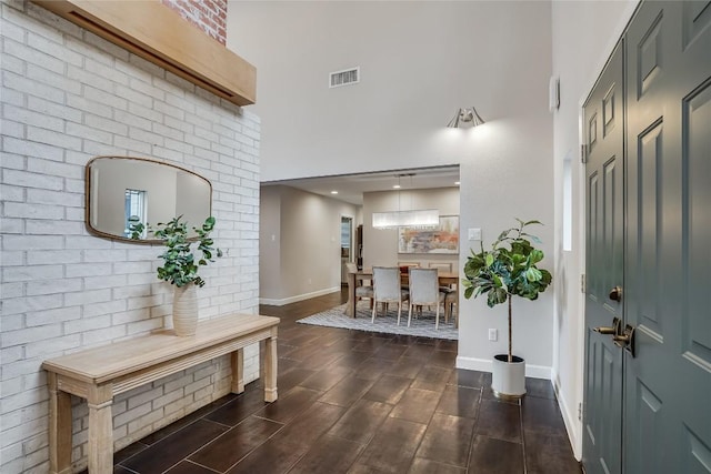 entryway with baseboards, a high ceiling, visible vents, and wood finish floors