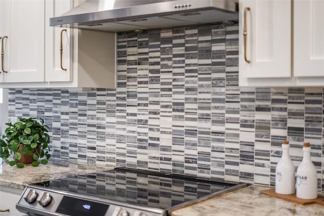 kitchen with light stone counters, white cabinets, decorative backsplash, and wall chimney exhaust hood