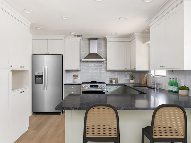 kitchen featuring a sink, white cabinets, appliances with stainless steel finishes, light wood-type flooring, and wall chimney exhaust hood