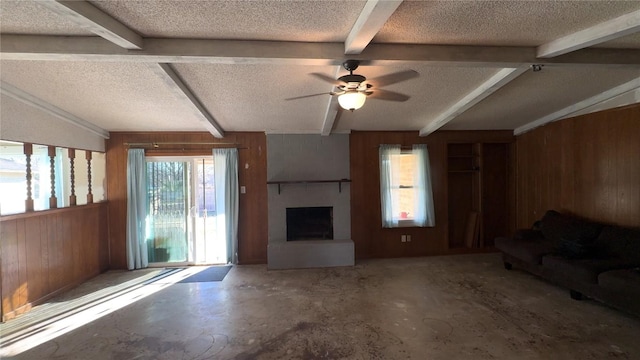 unfurnished living room with beam ceiling, a large fireplace, wood walls, a textured ceiling, and concrete floors