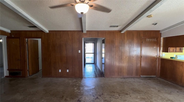 unfurnished room featuring visible vents, beamed ceiling, and wood walls