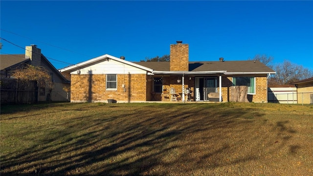 back of house with brick siding, a chimney, fence, and a lawn